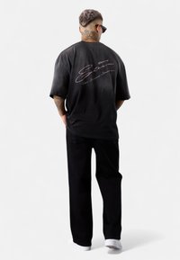 Black oversized t-shirt with faded effect, featuring pink cursive text on the back, paired with black pants and white shoes.