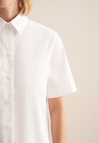 Hvid kortærmet skjorte med knappelukning og spids krave, lavet af glat stof, med seks knapper ned ad fronten og en afslappet pasform.