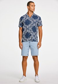 Camisa de botones de manga corta en navy con patrón floral blanco combinada con shorts de mezclilla celeste y zapatillas blancas.