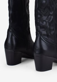 Botas de cuero negro hasta la rodilla con bordados decorativos en negro, tacones bajos y cremalleras laterales para facilitar su uso.