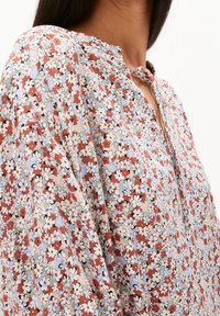 Chemisier fleuri en tissu léger avec un motif multicolore de fleurs rouges, bleues et blanches, doté d'un décolleté en V et de manches froncées.