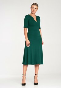 Zielona sukienka do kolan z krótkimi rękawami, dopasowanym góry i rozkloszowanym dołem. Wykonana z teksturowanej tkaniny, ma subtelny dekolt w kształcie litery V.