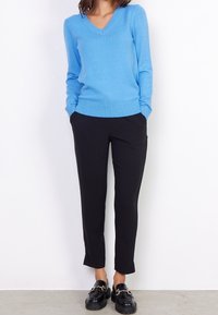 Hellblauer V-Ausschnitt-Pullover aus weichem Strickstoff, kombiniert mit schwarzen, enger werdenden Hosen und klobigen schwarzen Slippern mit einer Kettenakzent.