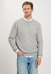 Szara bluza z okrągłym dekoltem i prążkowanymi mankietami, nałożona na białą koszulę w kropki. Styl casualowy, miękka tekstura.