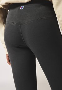 Zwarte geribbelde legging met een hoge tailleband, voorzien van geborduurde logo-details en zichtbare stiksels, ontworpen voor een nauwsluitende pasvorm.