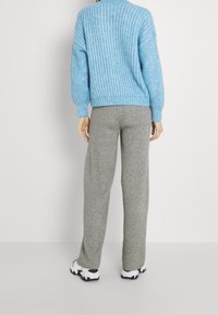 Světlomodrý pletený svetr s texturovaným vzorem, kombinovaný se šedými tepláky a bílými teniskami. Oblečení má volný střih.