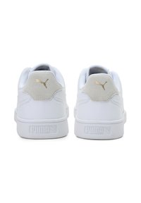 Bílé tenisky s hladkým koženým svrškem, polstrovaným límcem a šedou semišovou akcentací na patě. Zlaté logo Puma na patě a jazyku.