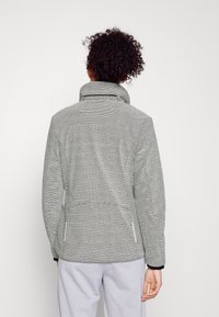 Graue, strukturierte Fleecejacke mit hohem Kragen, seitlichen Taschen und dunkler Einfassung. Sie hat ein dezentes Muster und eine figurbetonte Form.