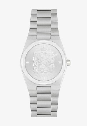 Reloj plateado con una pulsera de acero inoxidable texturizada, caja octagonal y esfera grabada con letras estilizadas. Acabado cepillado sutil en toda la pieza.