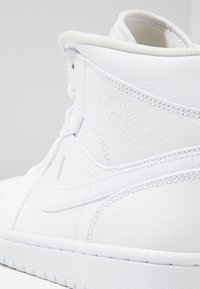 Vita hög-top-sneakers i texturerat läder med en slät yta, prydda med Air Jordan-logotypen präglad på sidan och vita snören.