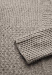 Ljusgrå stickad tröja med varierade texturer: ribbade sektioner, ett honungskake-mönster och en mjuk, fluffig yta.