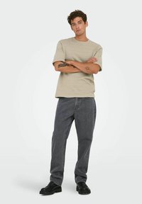 Beige gestructureerd kortermig shirt met een ronde halslijn, gecombineerd met loszittende grijze jeans en zwarte veterschoenen.