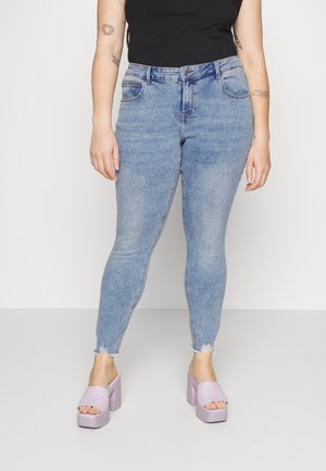 Persona que lleva vaqueros ajustados azul claro con bajos deshilachados, una camiseta sin mangas negra y sandalias de plataforma lavanda.