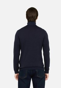 Maglione a collo alto blu navy realizzato in tessuto morbido, con maniche lunghe e design aderente, abbinato a jeans in denim scuro.