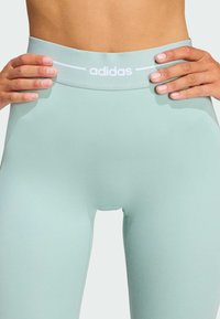 Ljusblå träningsleggings med hög midja och slätt tyg, med en vit logotypdetalj på midjebandet.