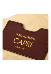 Étiquette en cuir marron Dolce & Gabbana avec texte doré « CAPRI Made in Italy » cousue sur un tissu beige.
