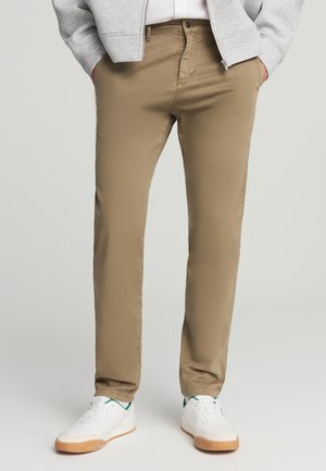 Pantaloni color khaki realizzati in cotone liscio con un design a gamba dritta. Presentano passanti per cintura, tasche davanti e sono abbinati a scarpe da ginnastica bianche.