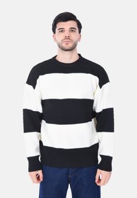 Maglione a righe bianche e nere con un motivo a maglia testurizzato. Design classico con collo a giro e polsini e orlo a coste.