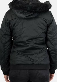 Sort polstret jakke med hætte foret med imiteret pels, ribstrikkede manchetter og kant. Glat tekstur og afslappet pasform, egnet til koldt vejr.
