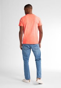 Maglietta a maniche corte e colletto rotondo di un vivido corallo, abbinata a jeans di denim azzurro chiaro. Presenta una vestibilità rilassata e un tessuto morbido e testurizzato.