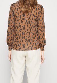 Braunes Tiermuster-Oberteil mit schwarzen, leopardähnlichen Punkten, langen Ärmeln mit gerafften Bündchen, aus einem strukturierten, leichtgewichtigen Material gefertigt.