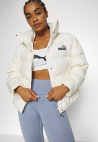 Puff jacket in off-white, quilted design with high collar and black logo; paired with light blue leggings featuring a black logo.