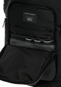 Interior de una mochila negra con un patrón de textura en panal, que presenta un compartimento con cremallera, etiqueta de marca y un acento de malla.