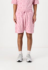 Pink textured shorts with elastic waistband and drawstring, featuring a repeated logo pattern. Worn with white ankle socks and sneakers.