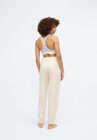 Sujetador deportivo de rayas gris claro con diseño de espalda de nadadora, combinado con pantalones de chándal crema, suaves y de corte relajado. Pies descalzos visibles.