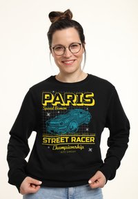 Zwarte sweatshirt met een grafische print van een blauwe auto met "PARIJS" en "STREET RACER Kampioenschap" in vetgedrukte gele letters. Katoenen materiaal.