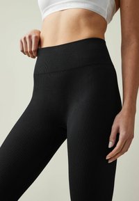 Sorte ribbede leggings med højt talje, der har et tekstureret stof og glat finish. Nærbillede fremhæver taljebåndet og pasformen.