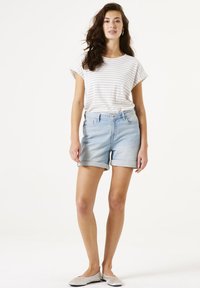 Camisa de rayas de manga corta en blanco y azul claro, combinada con pantalones cortos de mezclilla azul claro. Los pantalones cortos tienen dobladillos enrollados y bolsillos frontales.