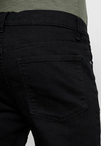 Svarta denimjeans med en slät textur, med en bakficka som har subtila sömnadsdetaljer och ett midjeband som sitter nära kroppen.