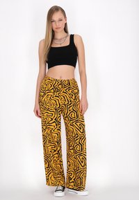 Svart ribbat crop top i kombination med gula vida byxor med ett svart abstrakt mönster. Modellen bär svarta sneakers.