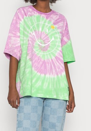 Koszulka z krótkim rękawem, w luźnym fasonie, w kolorze tie-dye w odcieniach zieleni i fioletu, z białą grafiką uśmiechniętej buźki oraz żółtą przypinką w kształcie uśmiechniętej buźki.
