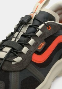 Μαύρο και γκρι αθλητικό παπούτσι με πορτοκαλί λεπτομέρειες, υφασμάτινη υφή, ελαστικά κορδόνια και διαμορφωμένη σόλα. Διαθέτει λογότυπο Vans και κλείσιμο με κουμπί.