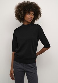 Suéter negro de manga corta con un cuello alto, hecho de material texturizado. Presenta un corte relajado y un dobladillo acanalado, combinado con jeans grises.