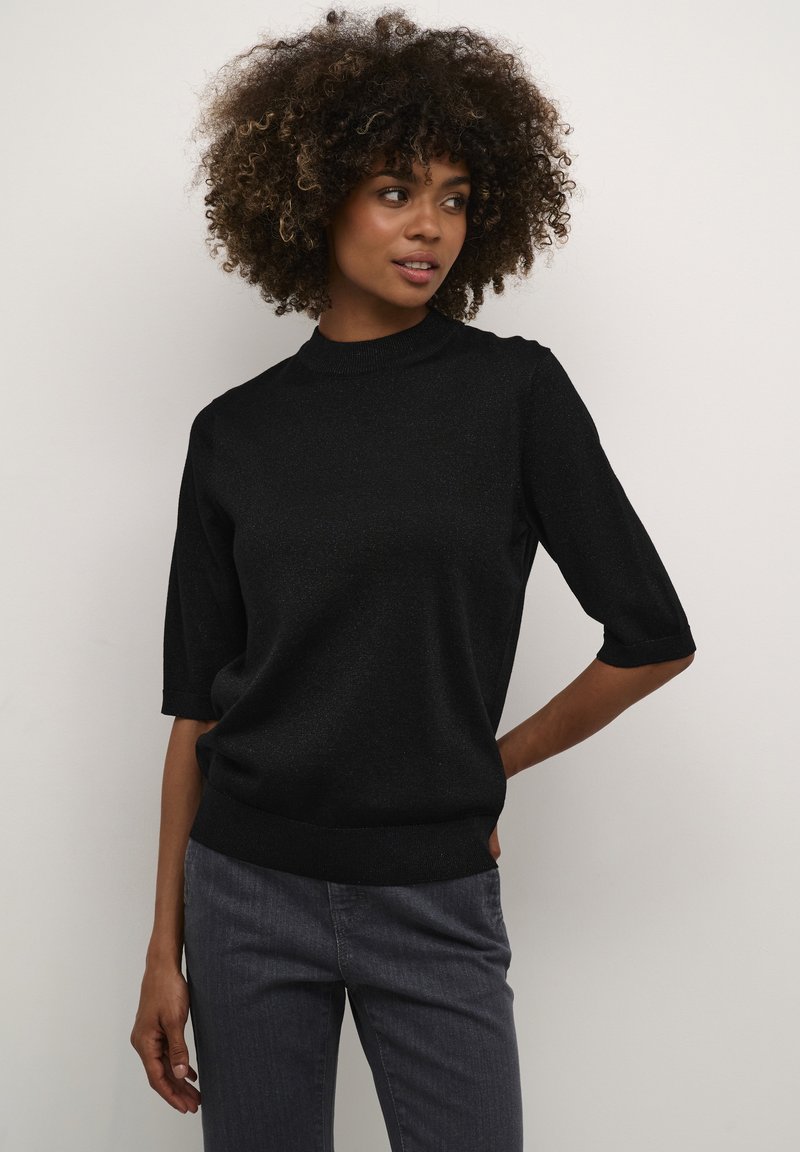 Suéter negro de manga corta con un cuello alto, hecho de material texturizado. Presenta un corte relajado y un dobladillo acanalado, combinado con jeans grises.