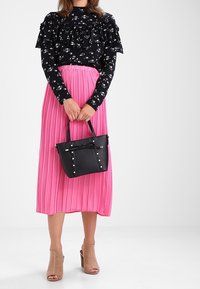 Sort blomstret bluse med flæser, plisseret pink midi-skirt, sort håndtaske med nitter og beige perforerede hæl sandaler.