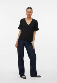 Top nero a scollo a V con maniche corte a volant, con chiusura davanti a bottoni. Abbinato a pantaloni in denim scuri a gamba larga e ballerine con fantasia.