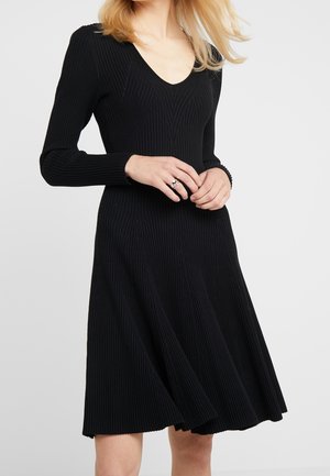 Vestito nero a coste con maniche lunghe e scollo a V; fondo della gonna svasato, tessuto testurizzato con linee verticali, lunghezza al ginocchio.