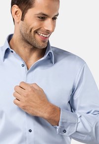 Lichtblauw overhemd met een gestructureerde kraag, gegedeelde binnenmanchetten en contrasterende knopen. Zachte stof met een gladde textuur.