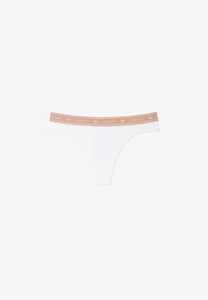 Tanga blanca de tela suave y elástica. Presenta una cinturilla de color naranja claro con la impresión en blanco de "LACOSTE". Diseño minimalista.