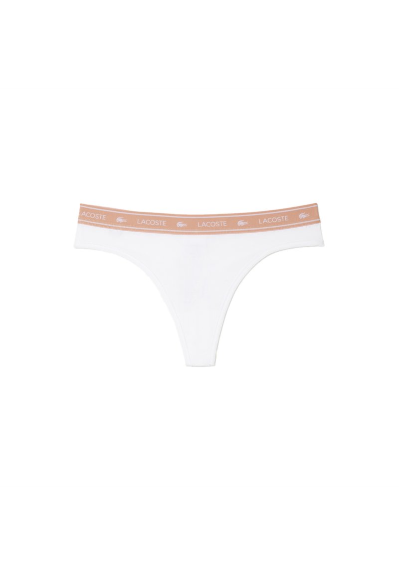 Tanga blanca de tela suave y elástica. Presenta una cinturilla de color naranja claro con la impresión en blanco de "LACOSTE". Diseño minimalista.