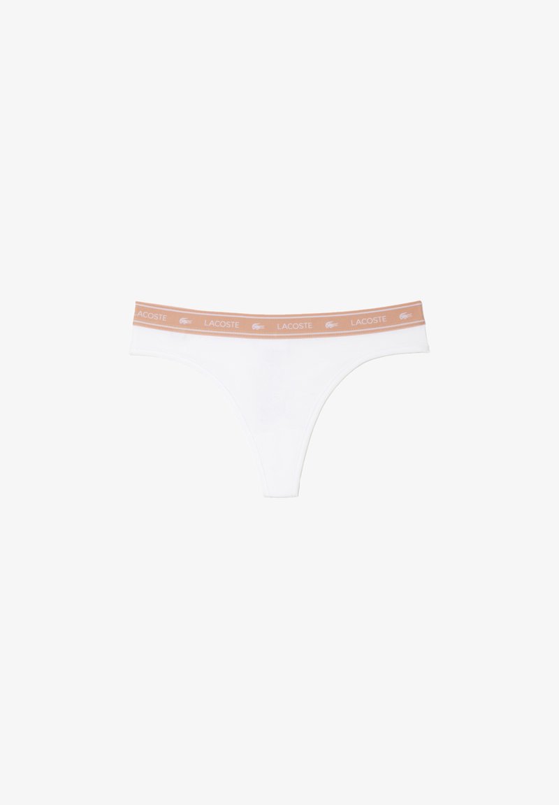 Tanga blanca de tela suave y elástica. Presenta una cinturilla de color naranja claro con la impresión en blanco de "LACOSTE". Diseño minimalista.