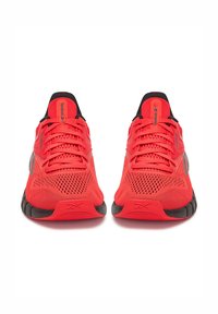 Heli punased spordijalatsid, millel on võrgusilmast ülemine osa, mustad aktsendid ja tekstuuriga tallad. Lõngad ja bränditud keel on ülaosas nähtavad.