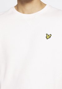 Felpa rosa chiaro con design a collo rotondo, dotata di un piccolo logo di un uccello giallo e nero sulla parte sinistra del petto. Texture del tessuto morbida.