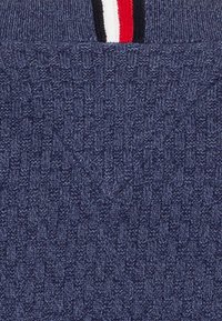 Granatowy dzianinowy sweter z fakturowanym wzorem tkanym. Posiada prążkowany kołnierz z czerwono-biało-czarnymi poziomymi paskami u góry.