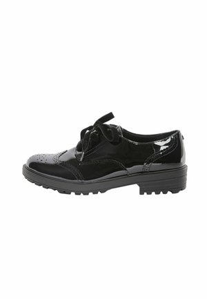 Schwarzer glänzender Schnür-Brogue-Schuh mit dekorativen Perforationen und klobiger Sohle, von der Seite auf weißem Hintergrund gesehen.