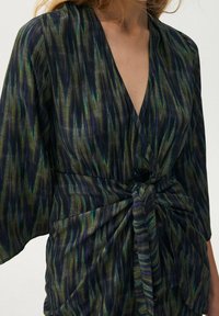 Mönstrad omslagstopp i mörka tyger, med vertikala ränder i gröna och blå nyanser, knuten i fronten och vida ärmar.